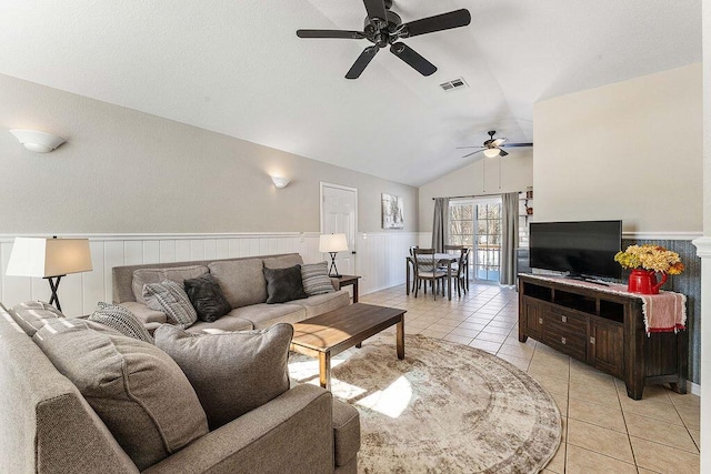 living room with light tile patterned floors, visible vents, a ceiling fan, wainscoting, and vaulted ceiling