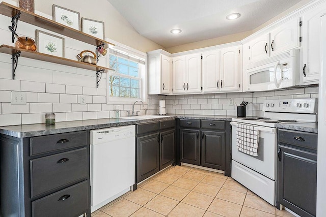 kitchen featuring dark countertops, white cabinetry, a sink, dark cabinets, and white appliances