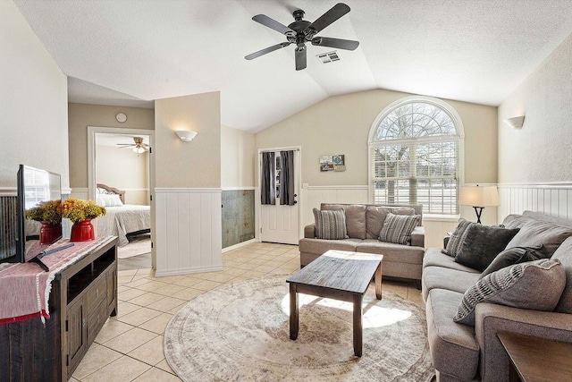 living area featuring a wainscoted wall, light tile patterned floors, visible vents, vaulted ceiling, and a textured ceiling