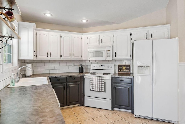 kitchen featuring dark countertops, white cabinetry, a sink, light tile patterned flooring, and white appliances