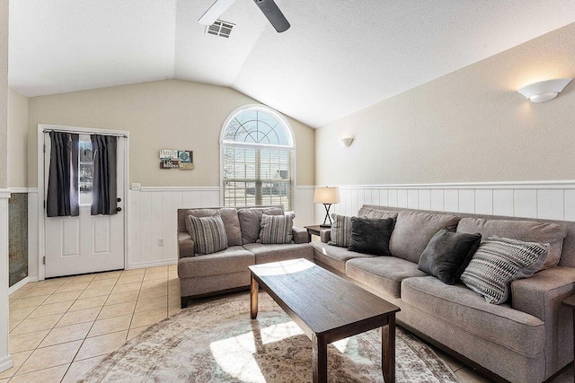 living room featuring light tile patterned floors, ceiling fan, visible vents, vaulted ceiling, and wainscoting