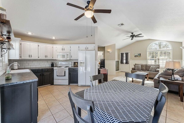 kitchen featuring white appliances, a sink, white cabinets, open floor plan, and dark countertops