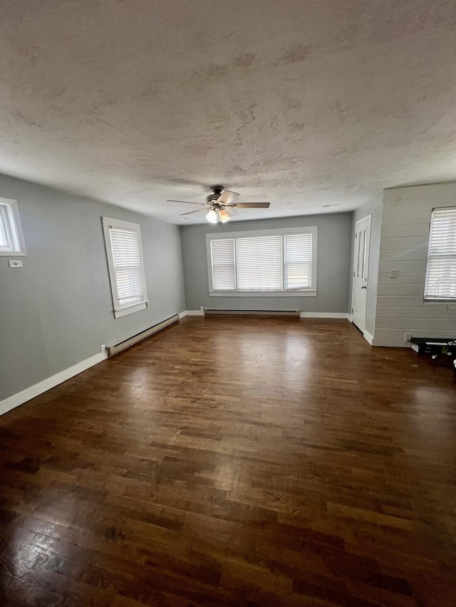 empty room with plenty of natural light, a textured ceiling, a baseboard heating unit, and dark wood-type flooring