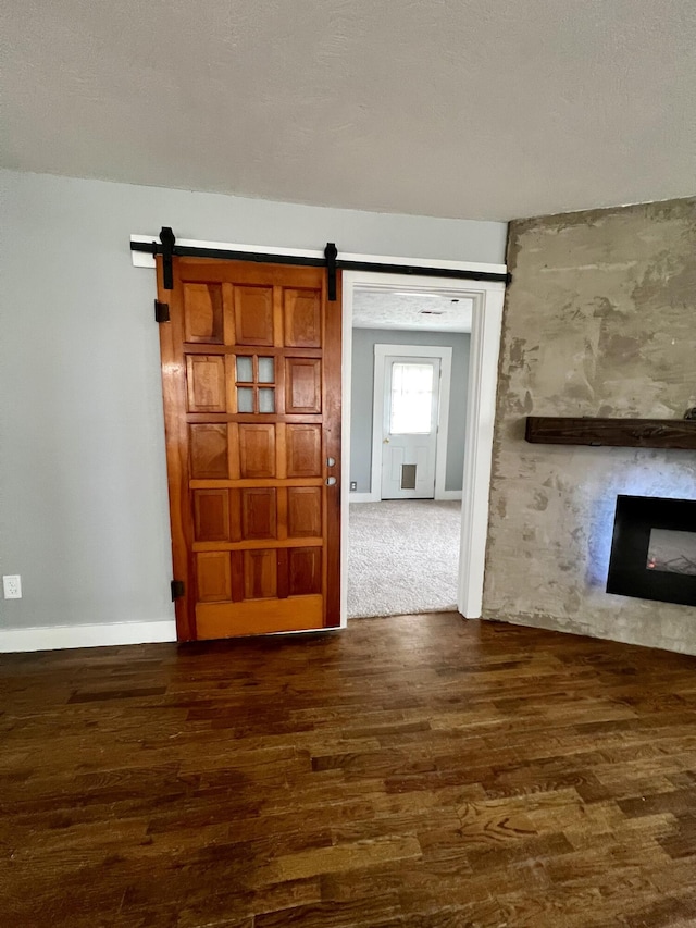 interior space with dark wood-style floors, a barn door, a fireplace, and baseboards