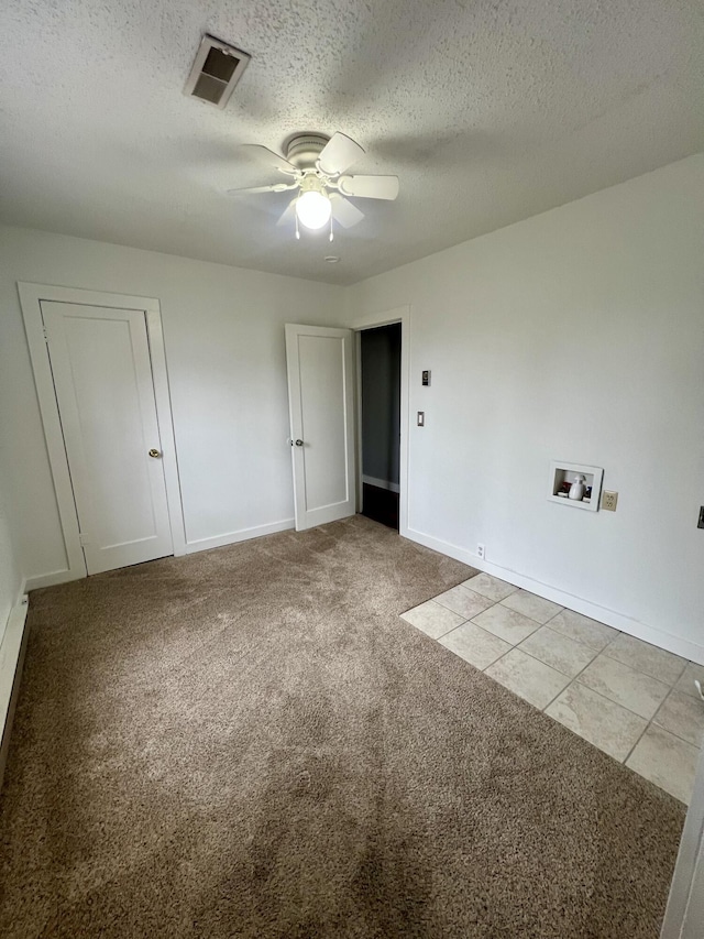 empty room featuring ceiling fan, a textured ceiling, light carpet, visible vents, and baseboards