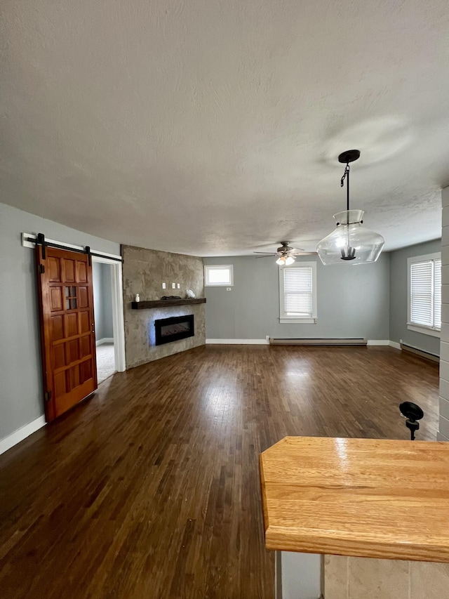 unfurnished living room with a wealth of natural light, dark wood-style flooring, baseboard heating, and a barn door