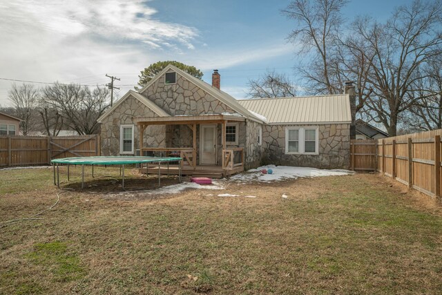 rear view of house with stone siding, a trampoline, a fenced backyard, and a chimney