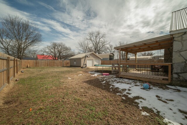 view of yard with a trampoline, a wooden deck, a fenced backyard, a garage, and an outdoor structure