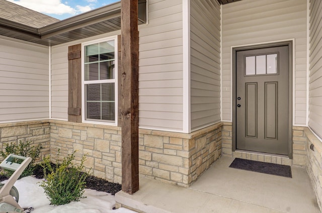 view of exterior entry featuring a shingled roof and stone siding