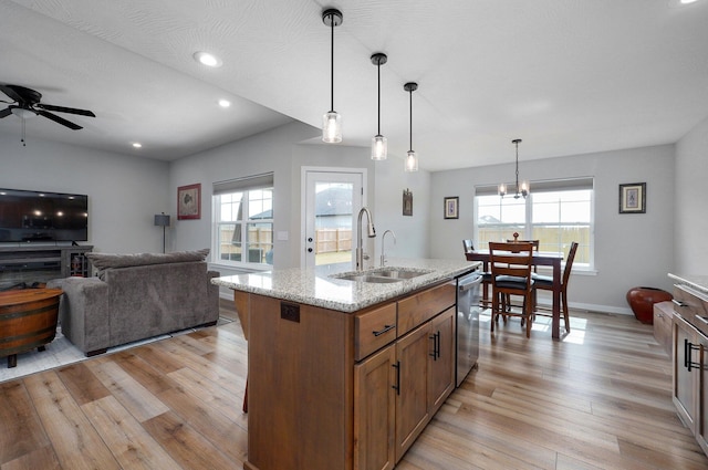 kitchen featuring an island with sink, decorative light fixtures, light stone countertops, stainless steel dishwasher, and a sink