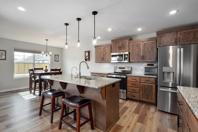 kitchen featuring appliances with stainless steel finishes, a kitchen island with sink, a sink, and hanging light fixtures