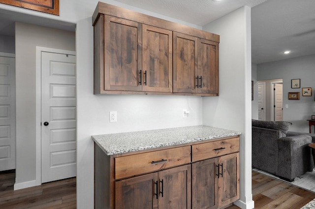 kitchen featuring open floor plan, light stone counters, dark wood finished floors, and baseboards