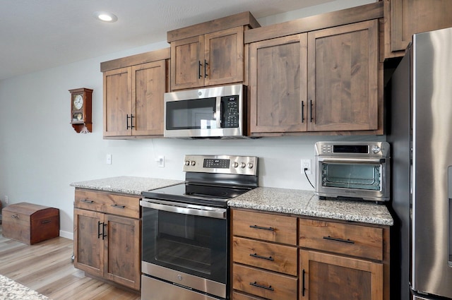 kitchen with light wood finished floors, a toaster, light stone counters, stainless steel appliances, and recessed lighting