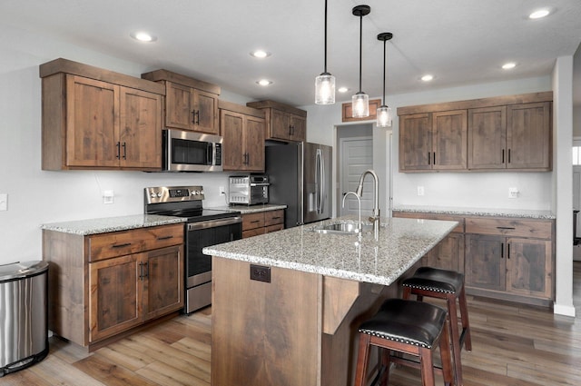 kitchen featuring stainless steel appliances, an island with sink, a sink, and light stone countertops