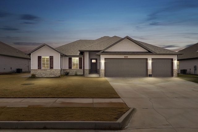 view of front of home with stone siding, central AC, an attached garage, and concrete driveway