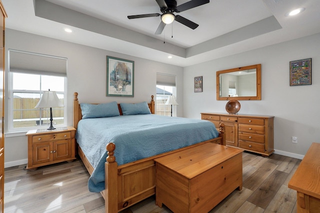 bedroom with recessed lighting, a raised ceiling, baseboards, and wood finished floors