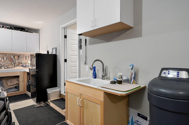 kitchen featuring a sink, white cabinetry, light countertops, freestanding refrigerator, and light brown cabinetry