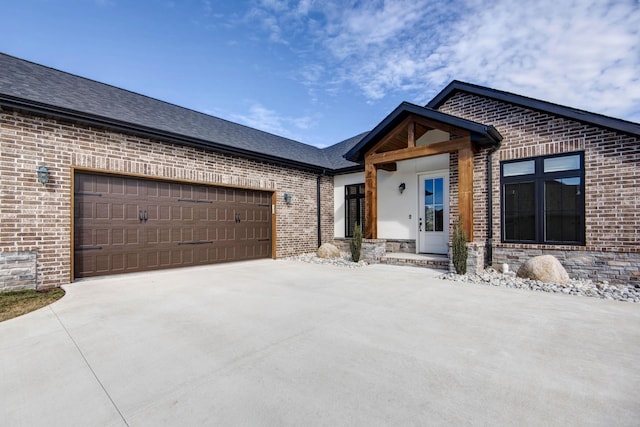 view of front of home with driveway, an attached garage, roof with shingles, and brick siding