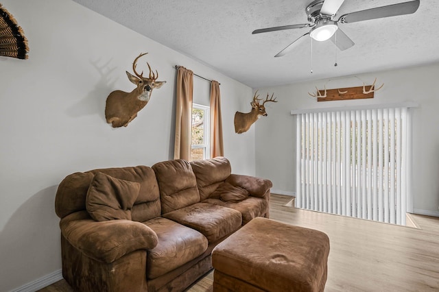 living room with a textured ceiling, baseboards, light wood-style flooring, and a ceiling fan