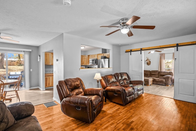 living area featuring a textured ceiling, a barn door, a ceiling fan, baseboards, and light wood-style floors