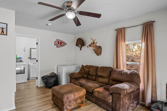 living room featuring light wood-style floors, a ceiling fan, washer / clothes dryer, and a textured ceiling