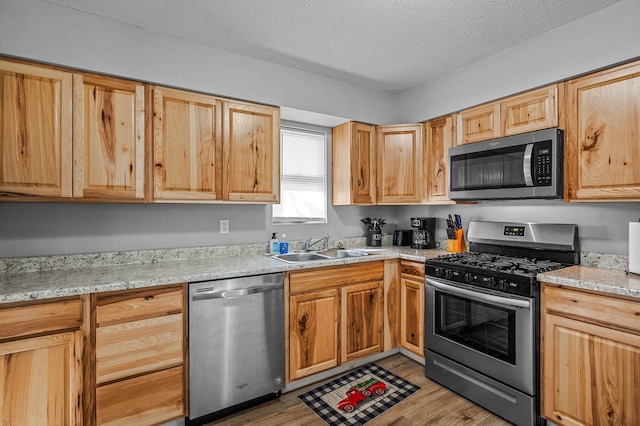 kitchen featuring a textured ceiling, light stone counters, a sink, light wood-style floors, and appliances with stainless steel finishes