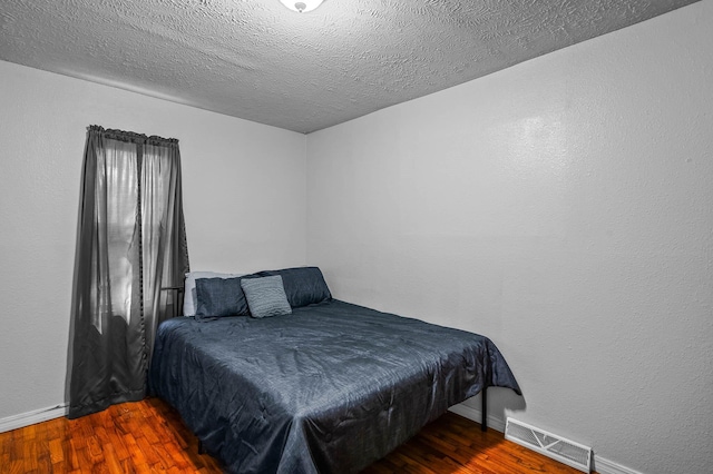 bedroom featuring a textured ceiling, wood finished floors, visible vents, and baseboards