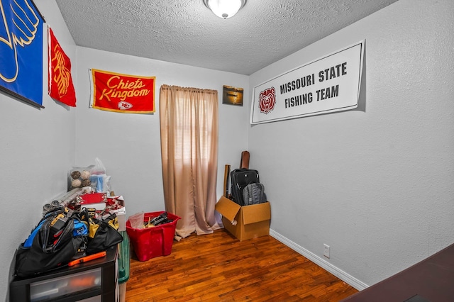 rec room with a textured ceiling, baseboards, and wood finished floors