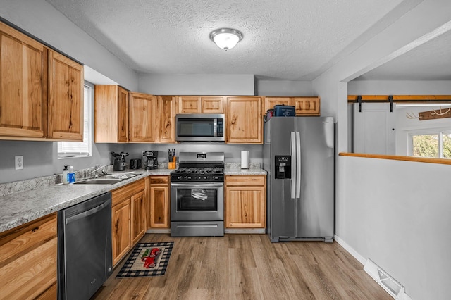 kitchen featuring visible vents, appliances with stainless steel finishes, a sink, a textured ceiling, and light wood-type flooring