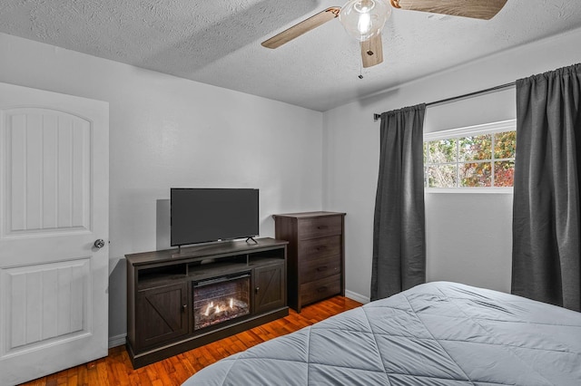 bedroom featuring baseboards, ceiling fan, light wood-style flooring, and a textured ceiling