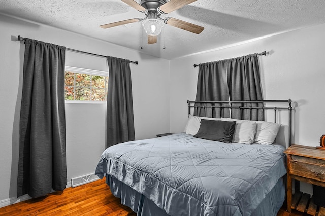 bedroom with a ceiling fan, a textured ceiling, visible vents, and wood finished floors