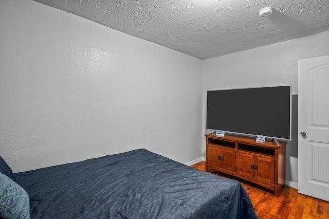 bedroom featuring a textured ceiling, baseboards, and wood finished floors