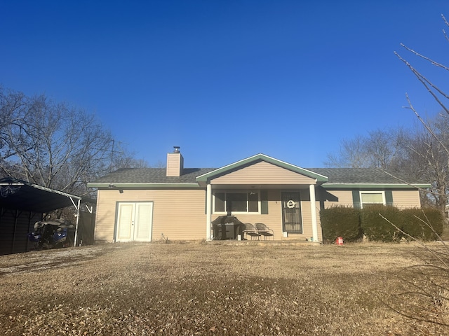 back of house with a carport, roof with shingles, and a chimney