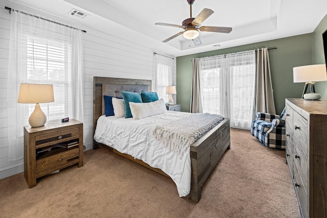 bedroom featuring a tray ceiling, visible vents, ceiling fan, and light carpet