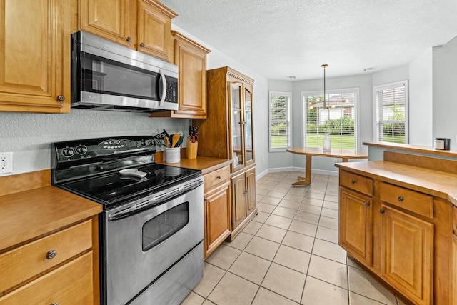 kitchen with decorative light fixtures, light countertops, appliances with stainless steel finishes, brown cabinetry, and light tile patterned flooring