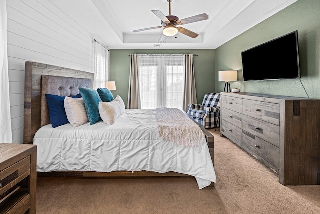 carpeted bedroom featuring wood walls, a raised ceiling, and a ceiling fan