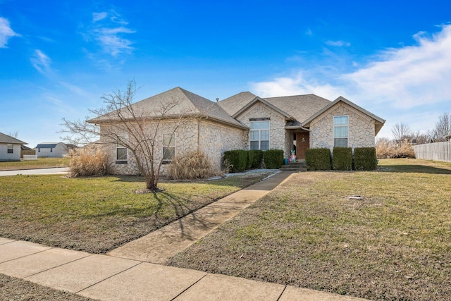 view of front of property featuring a front yard, stone siding, and roof with shingles