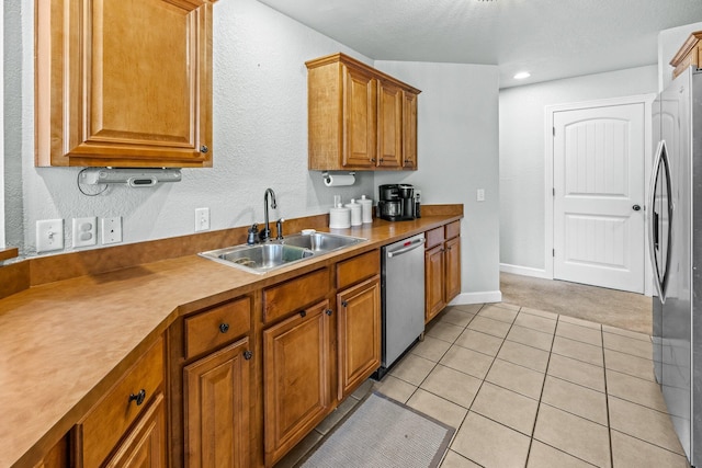 kitchen featuring light tile patterned floors, brown cabinets, stainless steel appliances, light countertops, and a sink