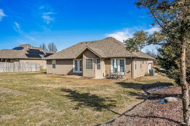 rear view of property featuring central air condition unit, a shingled roof, fence, and a lawn