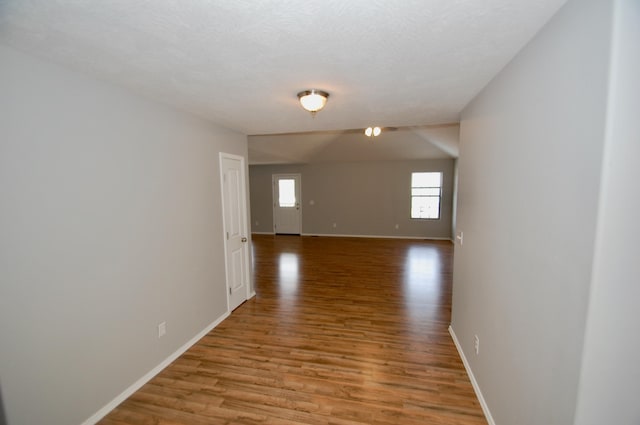 hallway with a textured ceiling, light wood-type flooring, and baseboards