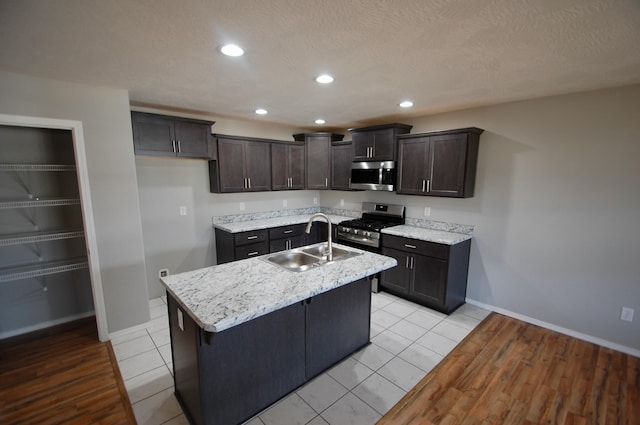 kitchen with a kitchen island with sink, recessed lighting, a sink, baseboards, and appliances with stainless steel finishes