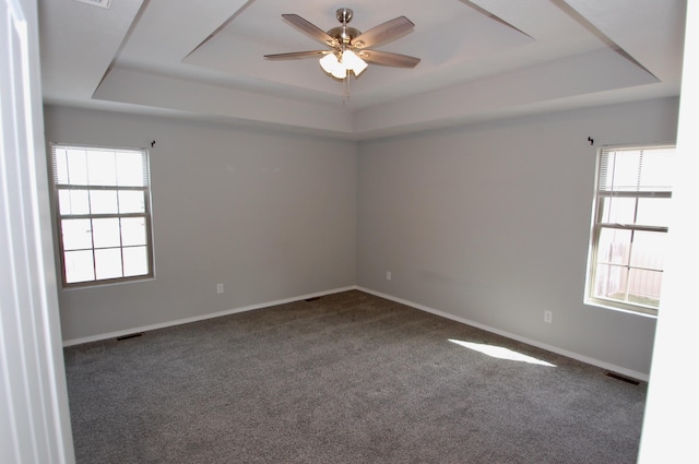 carpeted spare room featuring visible vents, a tray ceiling, a ceiling fan, and baseboards