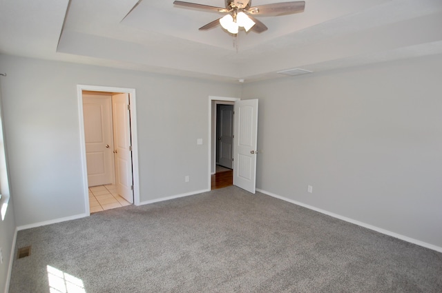 unfurnished bedroom with a tray ceiling, light colored carpet, visible vents, ceiling fan, and baseboards