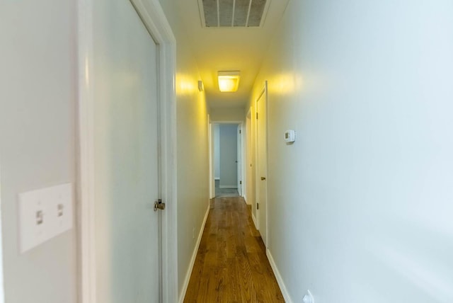 hallway with dark wood-type flooring, visible vents, and baseboards