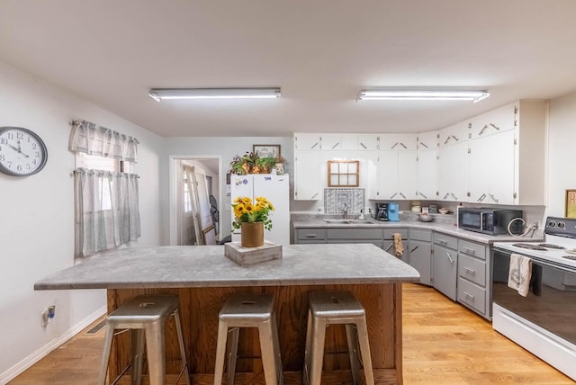 kitchen featuring light countertops, white appliances, gray cabinets, and a kitchen breakfast bar