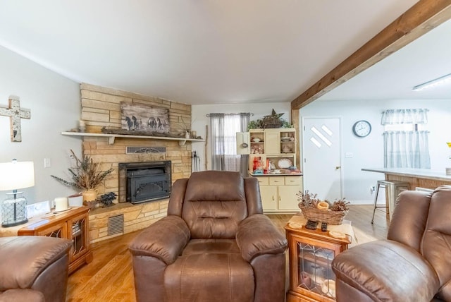 living area featuring light wood-type flooring, visible vents, beamed ceiling, and a stone fireplace