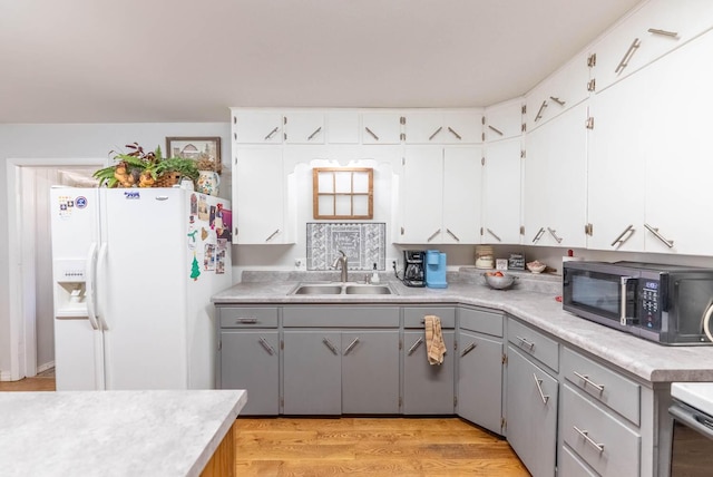 kitchen featuring stainless steel microwave, gray cabinets, light countertops, white fridge with ice dispenser, and a sink