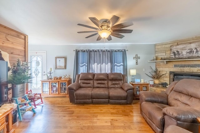 living area featuring ceiling fan, a stone fireplace, and light wood-type flooring