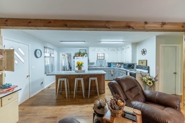 interior space with a center island, electric stove, stainless steel microwave, freestanding refrigerator, and beamed ceiling