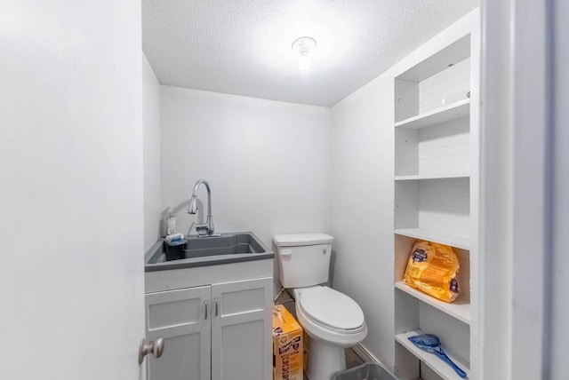 half bath with a textured ceiling, vanity, and toilet